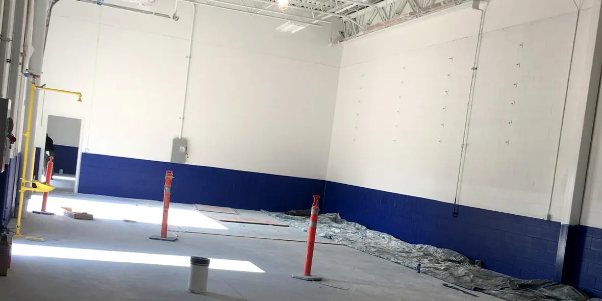 Warehouse interior with white painted walls and a blue painted band along the base, drop cloths and jack posts on the concrete floor