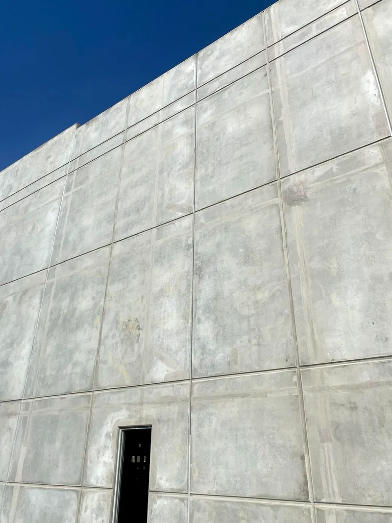 Close view of bare tilt-up concrete panels with visible filled joints and a dark door opening