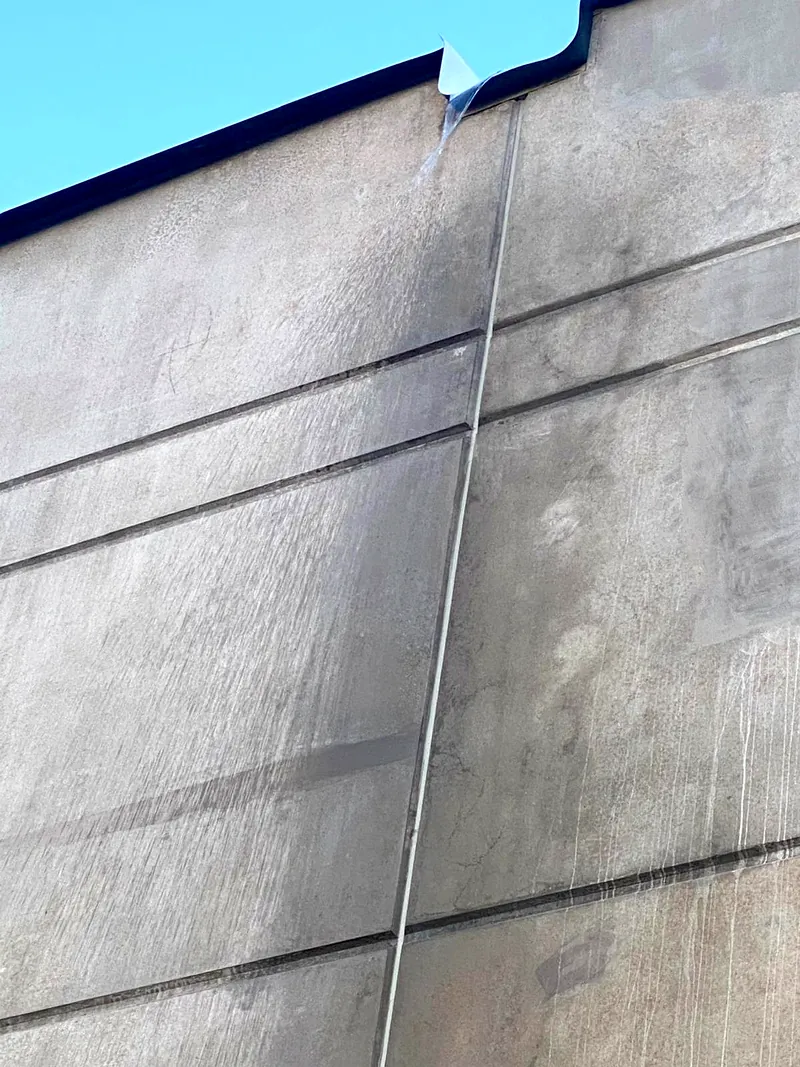 Bare concrete panels with dark runoff staining below a roof edge